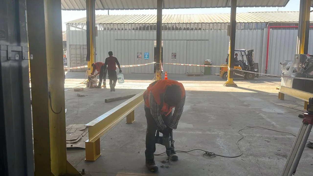 Trabajadores con chaleco reflectante instalando una barrera de acero amarilla dentro de un galpón industrial