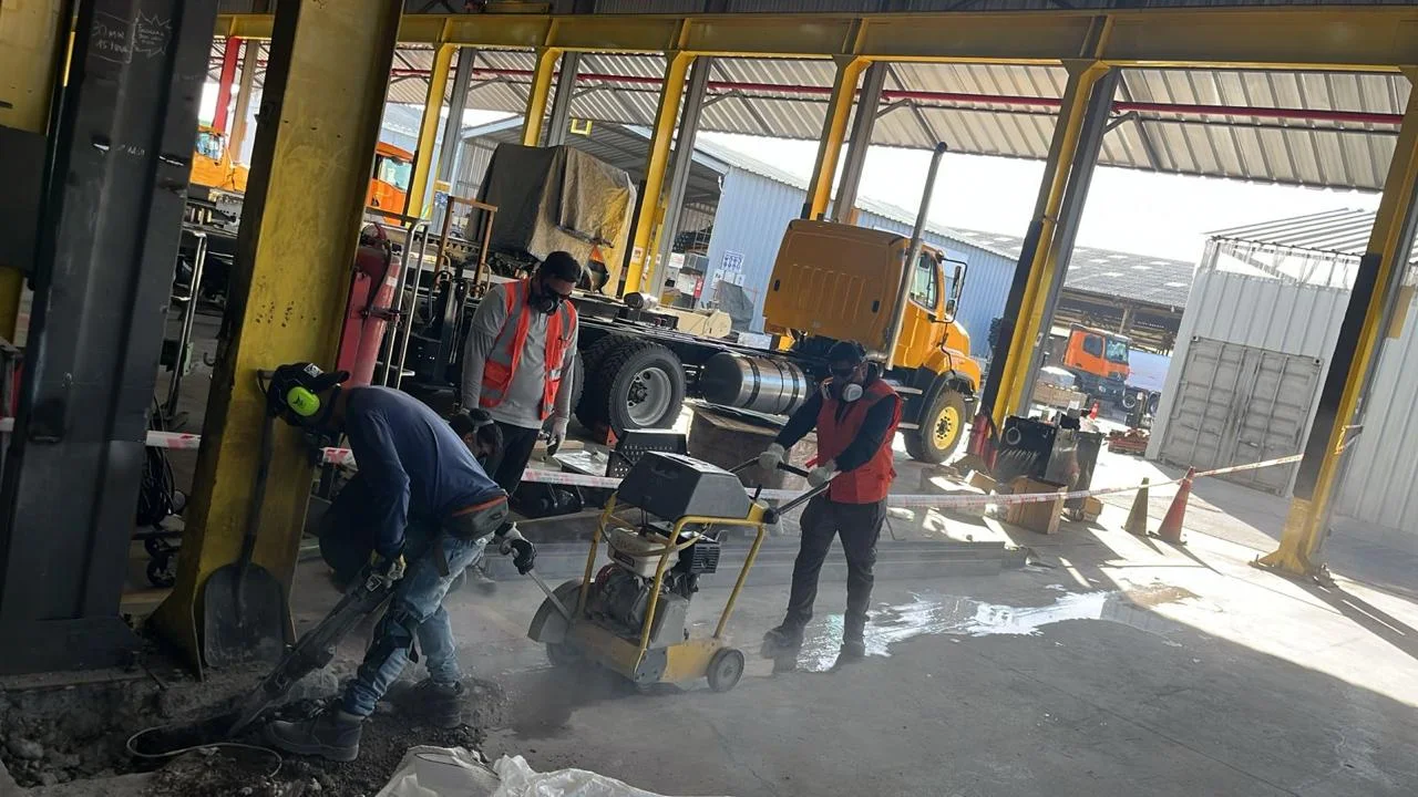 Equipo con protección respiratoria y auditiva cortando pavimento de hormigón con cortadora de piso en un galpón